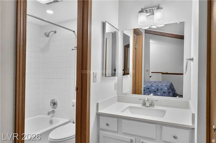 Bathroom featuring a white vanity with an integrated sink, brushed nickel faucet, and a wall-mounted mirror with a two-light fixture