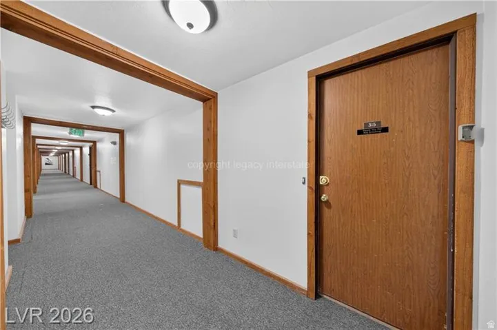 Solid wood-paneled door, brass hardware, wood-trimmed doorway, and wall-mounted light fixture