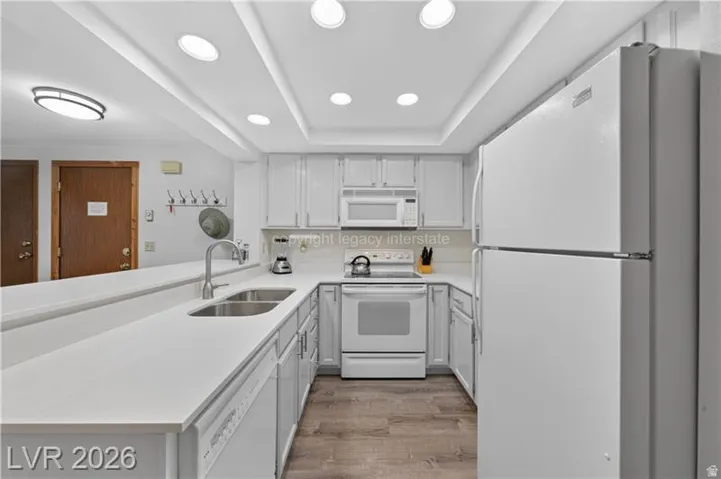 Kitchen featuring light-toned cabinetry, a double basin stainless steel sink, white appliances, recessed lighting, and wood-finish flooring