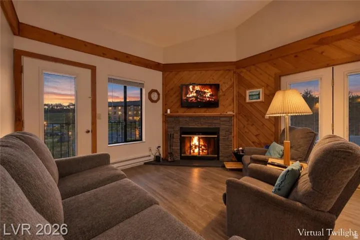 Slanted wood paneling, wood-finish flooring, stone-clad fireplace, and a vaulted ceiling