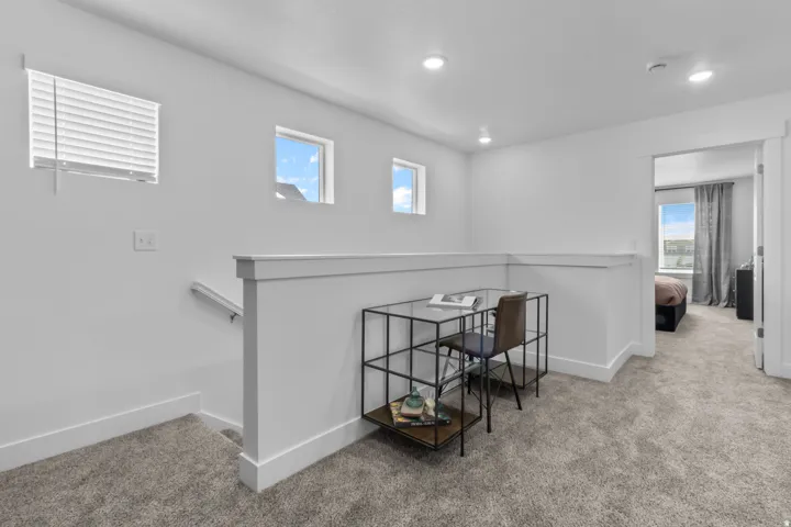 Carpeted landing with a half-wall railing, recessed lighting, and multiple windows