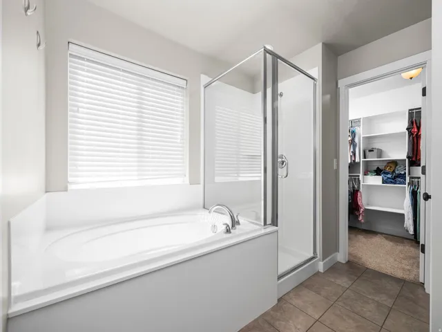 Soaking tub with a polished chrome faucet, glass-enclosed shower, and durable tile flooring