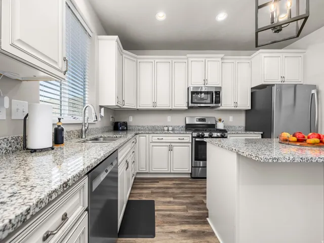 Kitchen featuring white cabinetry, granite countertops, wood-finish flooring, stainless steel appliances, and a built-in island