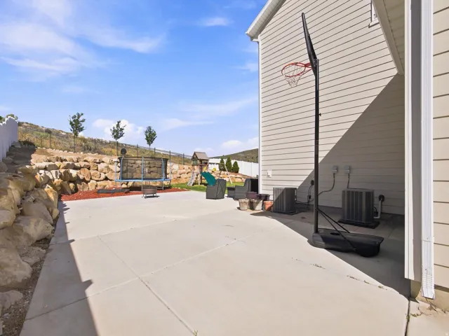 Concrete patio with a rock retaining wall, sloped landscaping, and vinyl siding