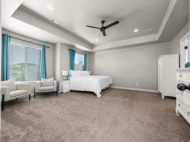 Spacious room featuring tray ceilings, recessed lighting, a ceiling fan, and carpet flooring