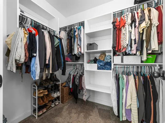 Walk-in closet with built-in shelving, multiple hanging rods, and neutral carpet flooring