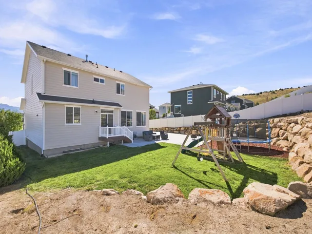 Expansive backyard featuring a manicured lawn, concrete patio, white vinyl fencing, and a terraced rock retaining wall