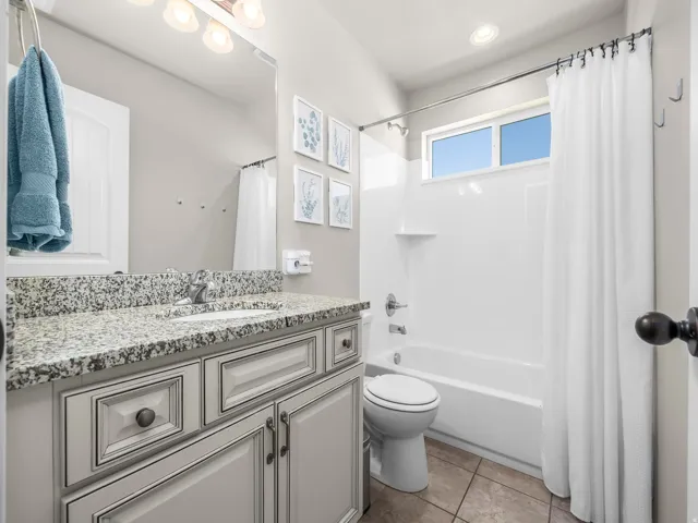 Bathroom featuring a vanity with a speckled countertop, a mirrored wall, a built-in tub with shower, and tile flooring