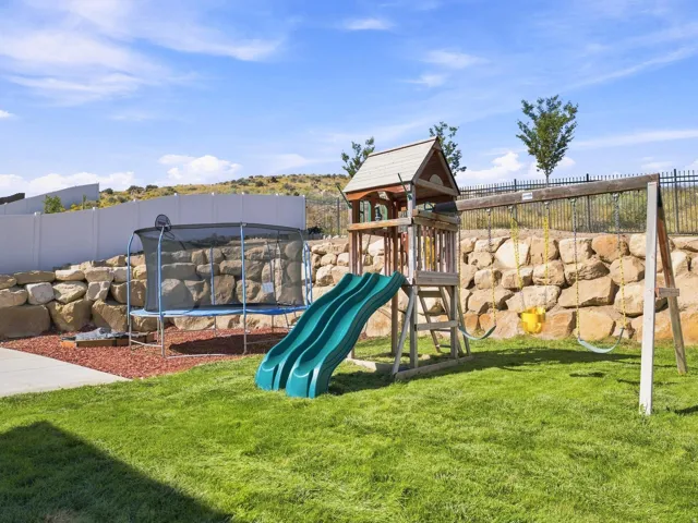 Expansive lawn area, natural rock retaining wall, white privacy fence, and a black wrought iron fence