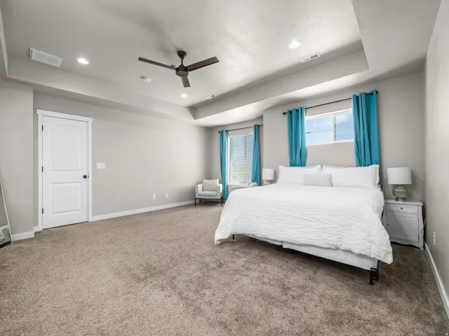 Tray ceiling with recessed lighting, ceiling fan, white interior door, and neutral carpeting
