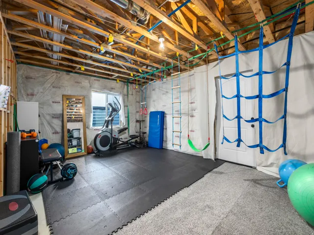 Exposed ceiling joists with visible ductwork, a permanent built-in climbing net, a permanent built-in climbing rope ladder, partial wall insulation, and a window