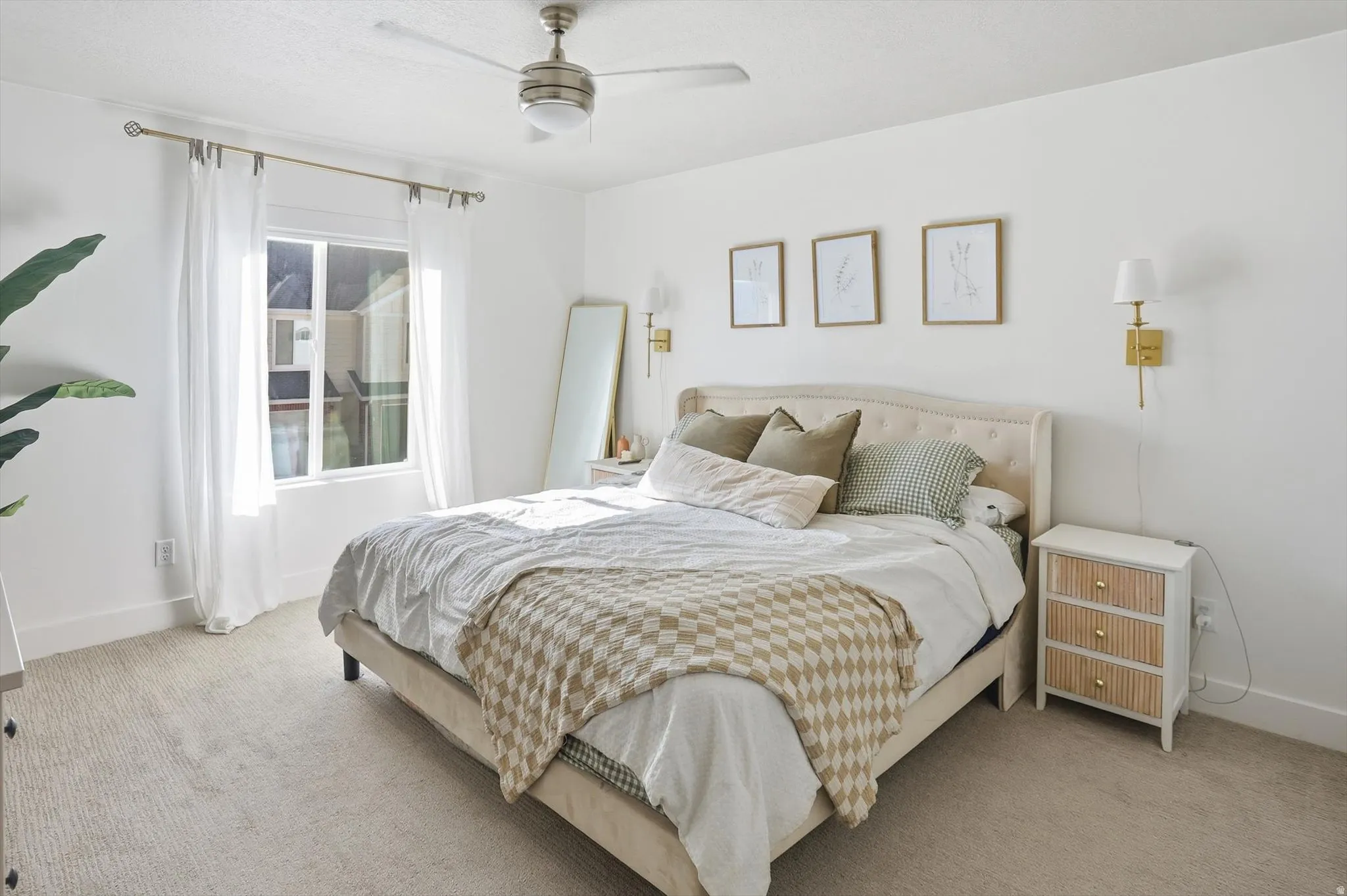 Recessed window with white drapes, ceiling fan with integrated lighting, wall-mounted sconces, and neutral tone carpeting