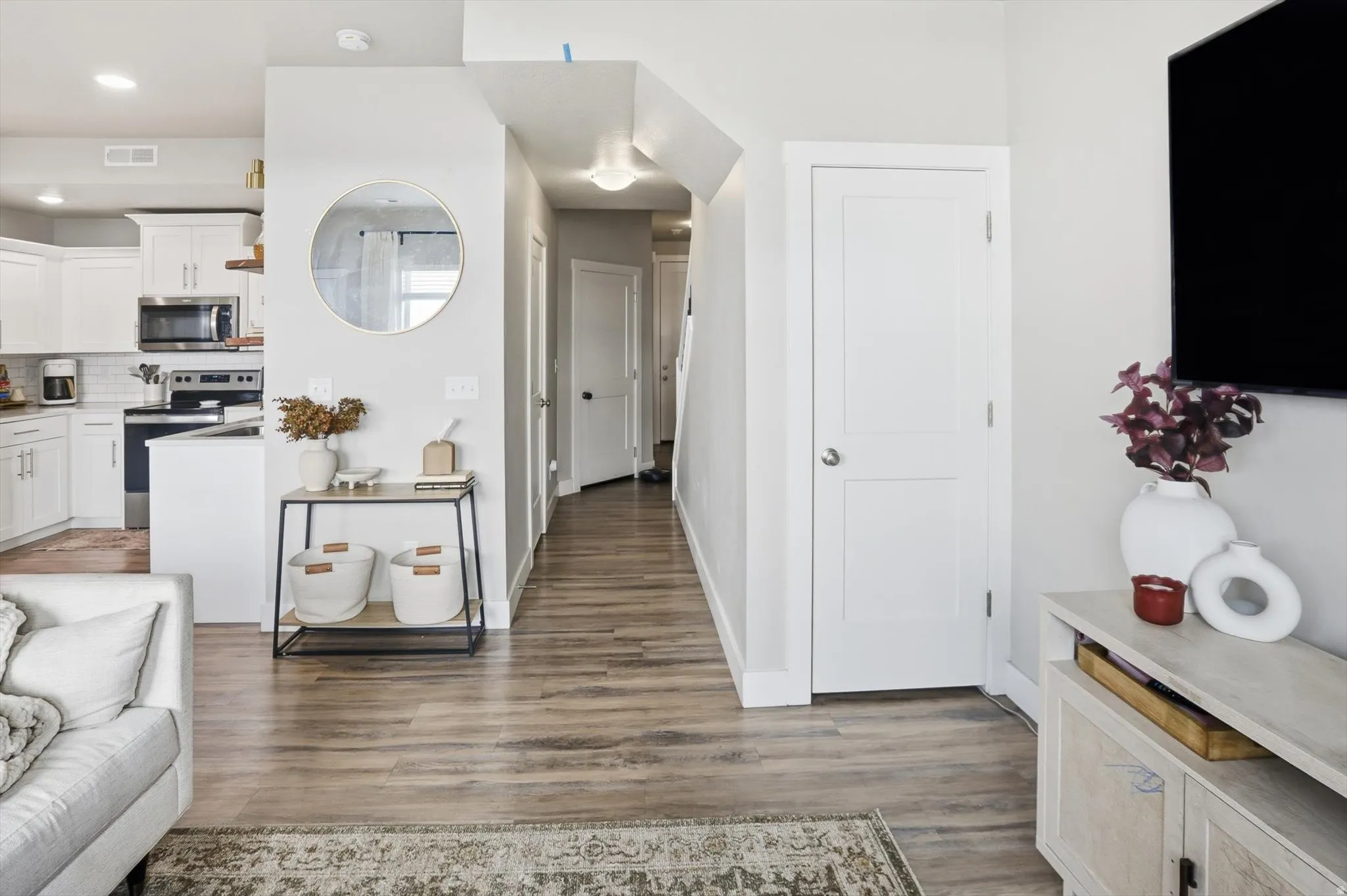Open-concept design featuring wood-finish flooring, white shaker cabinetry, stainless steel appliances, and a hallway with a panel door