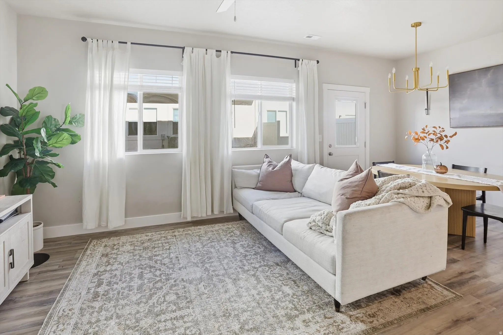 Open-concept living space featuring wood-finish flooring, multiple windows with blinds, a ceiling fan, and a gold-finish chandelier