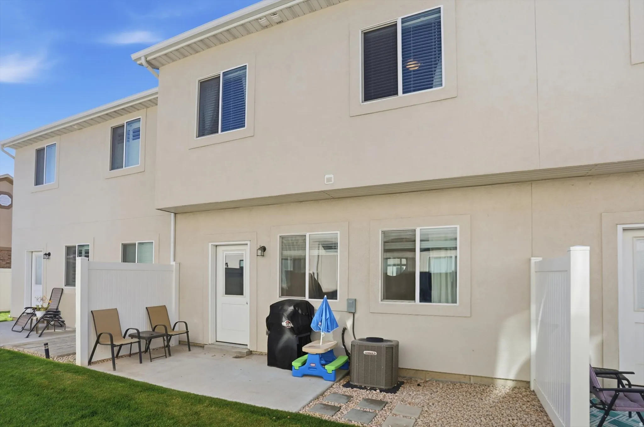 Rear exterior with a concrete patio, white vinyl fencing, stucco siding, and multiple windows
