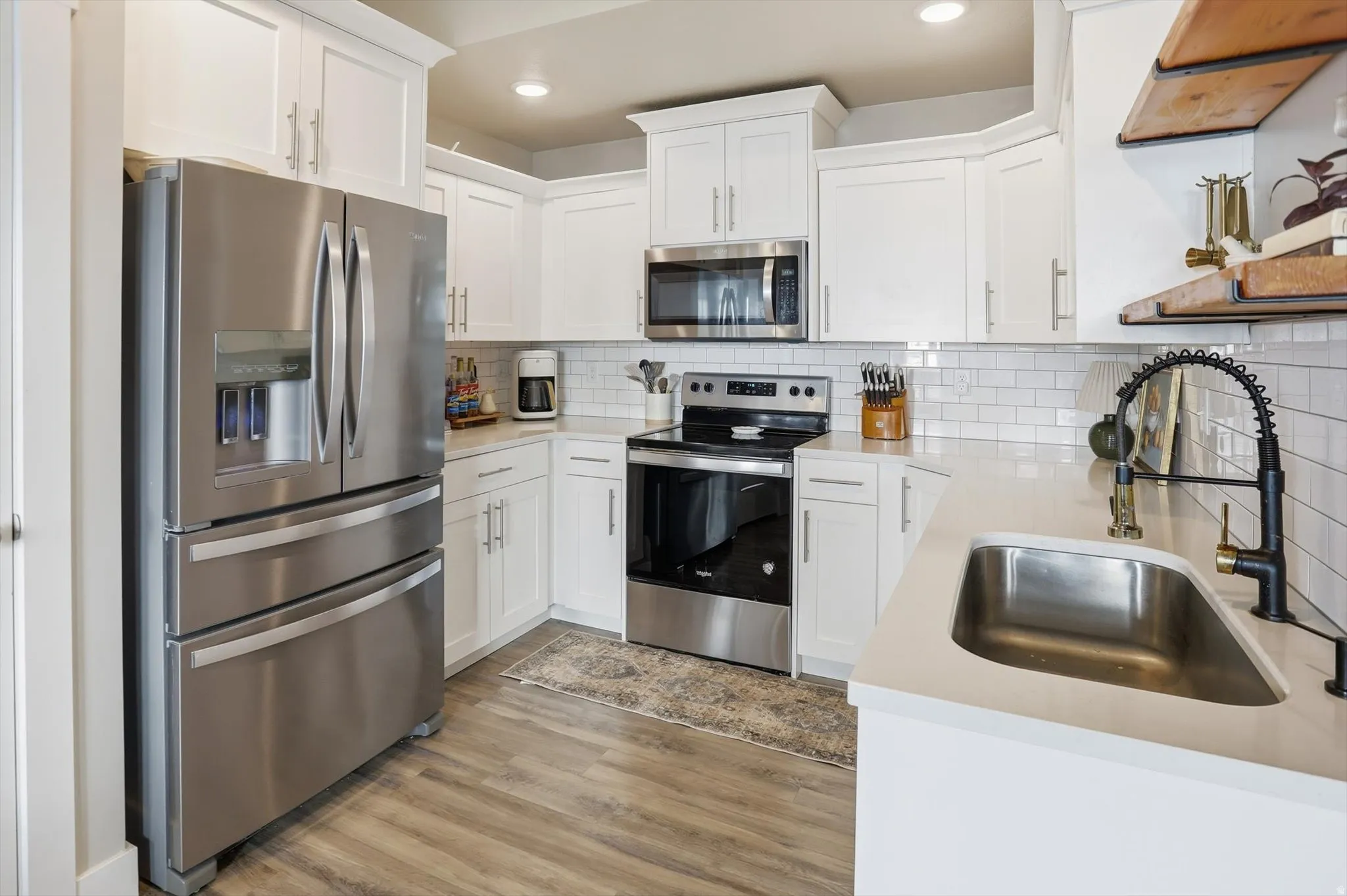White cabinetry with crown molding, stainless steel appliances, white subway tile backsplash, solid surface countertops, and wood-finish flooring