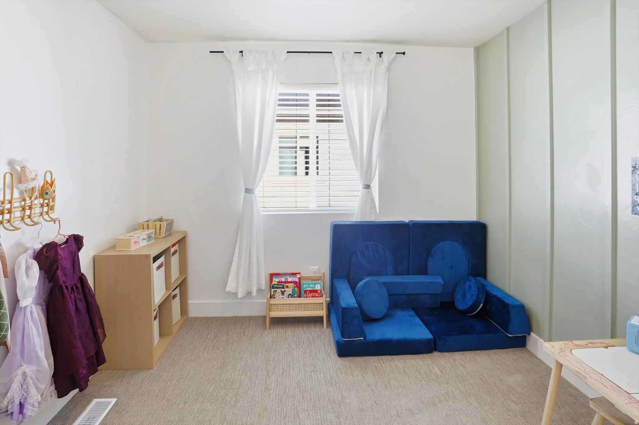 Wall-to-wall carpeting with a neutral tone, white walls, and a window with white blinds and curtains