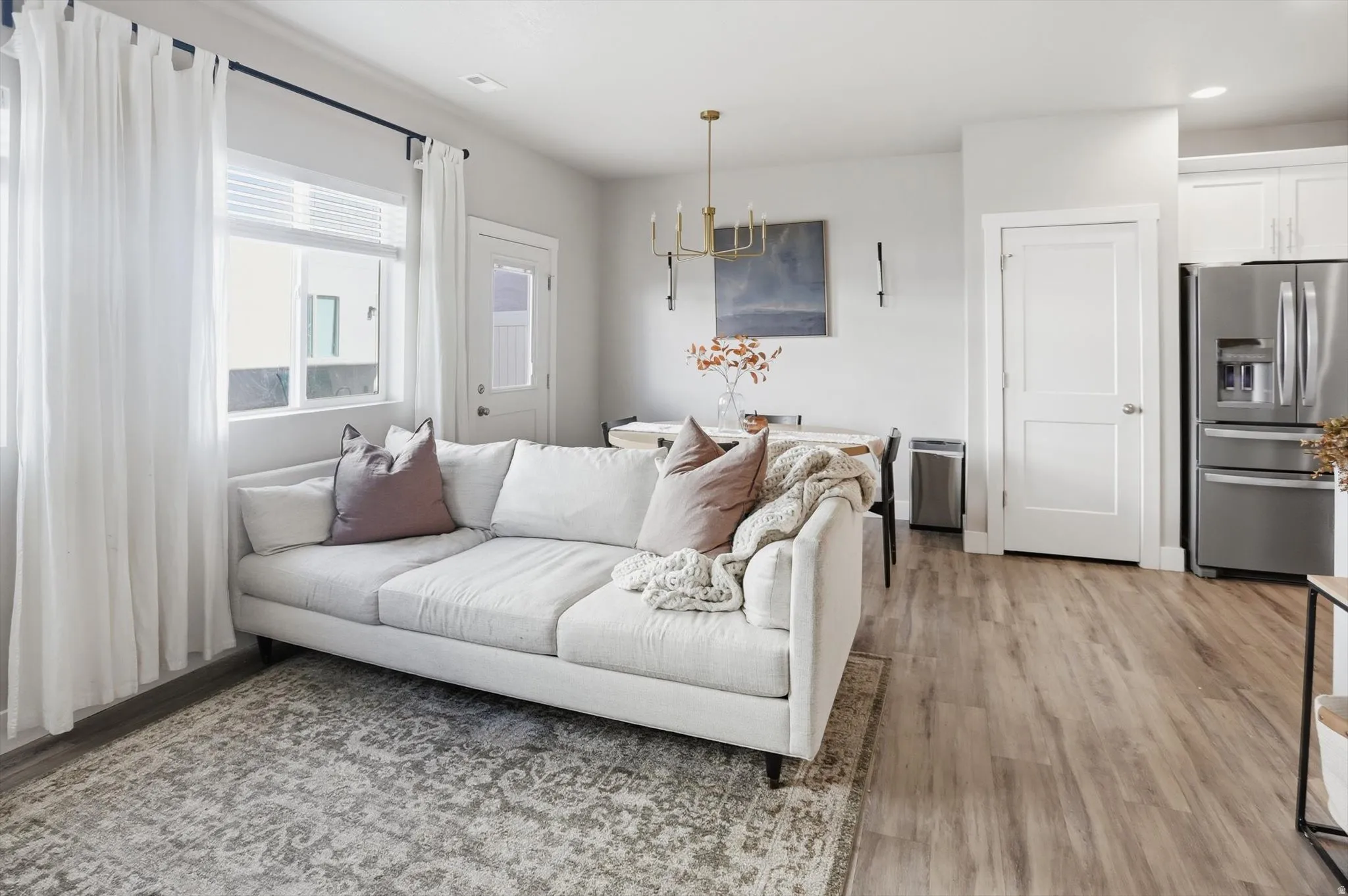 Wood-finish flooring throughout the living space, white shaker cabinetry, stainless steel refrigerator, and a brass-tone chandelier