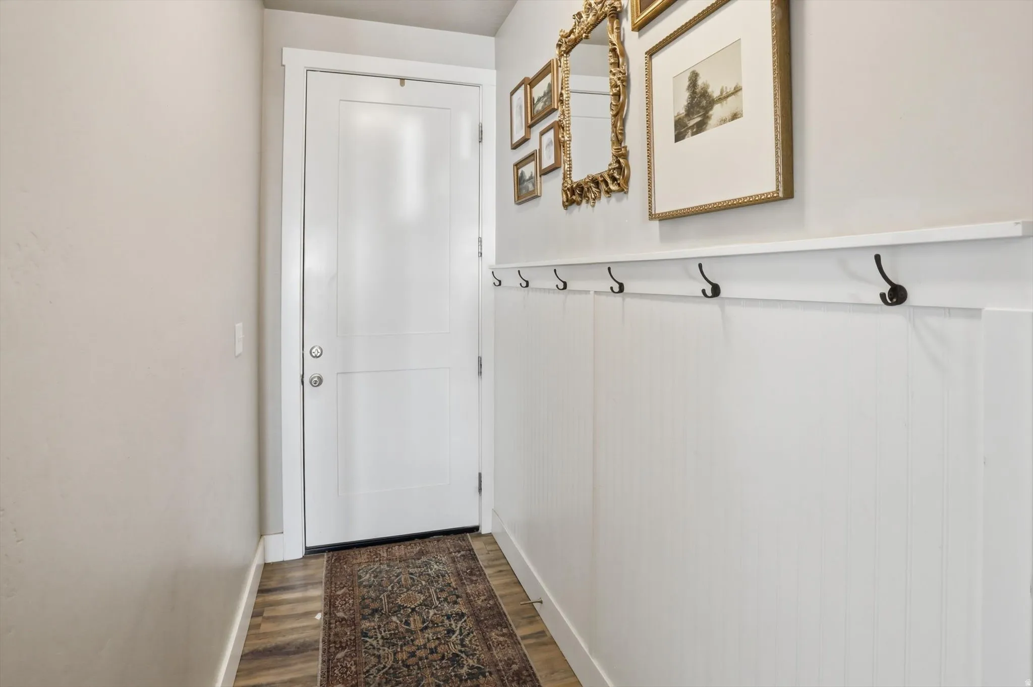 White paneled interior door, wood-finish flooring, and a white beadboard wall with integrated coat hooks