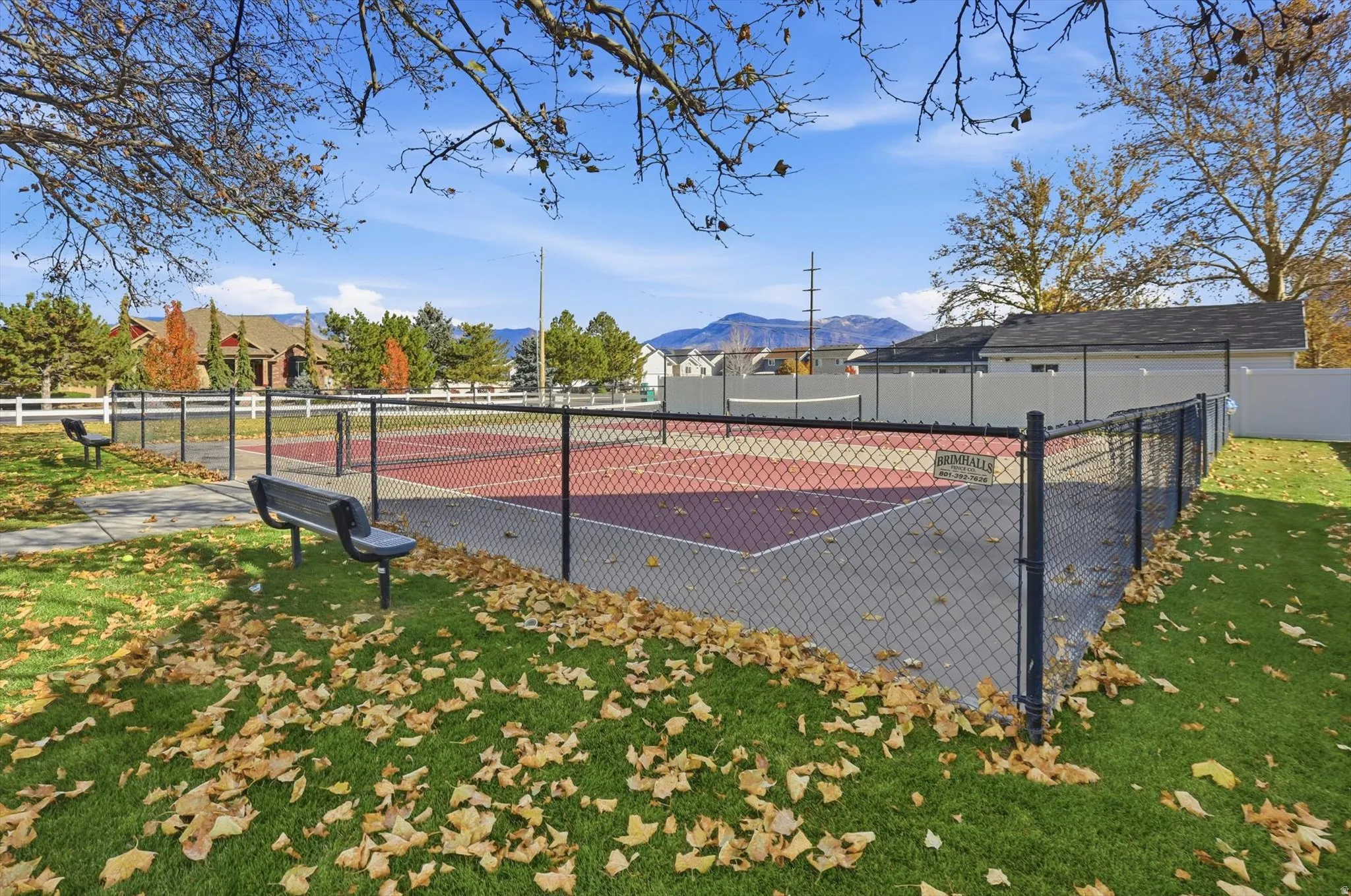 Fenced recreational court with an asphalt surface, surrounded by green lawn and paved walkways