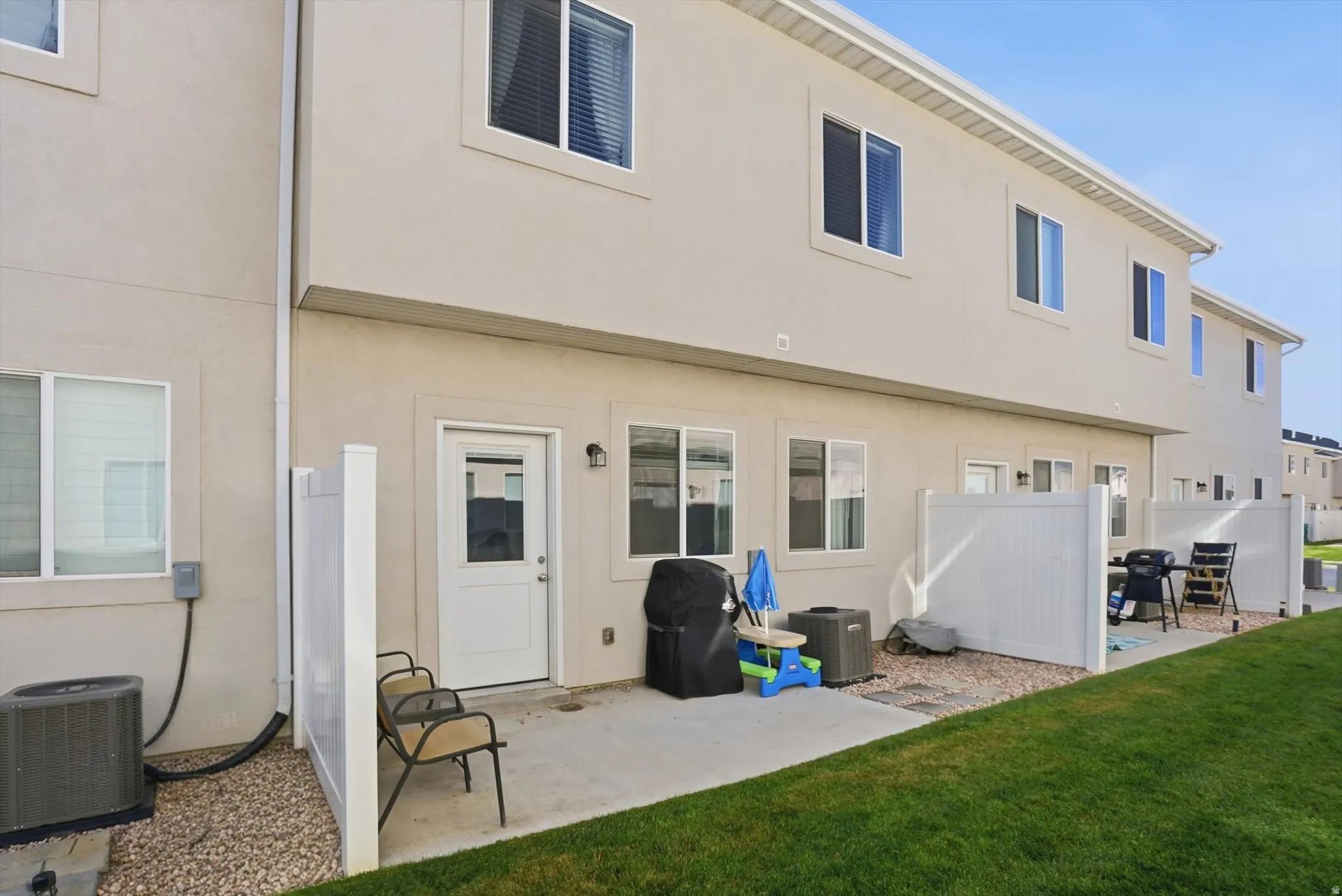 Rear patio with concrete slab, white privacy fencing, and adjacent grassy area