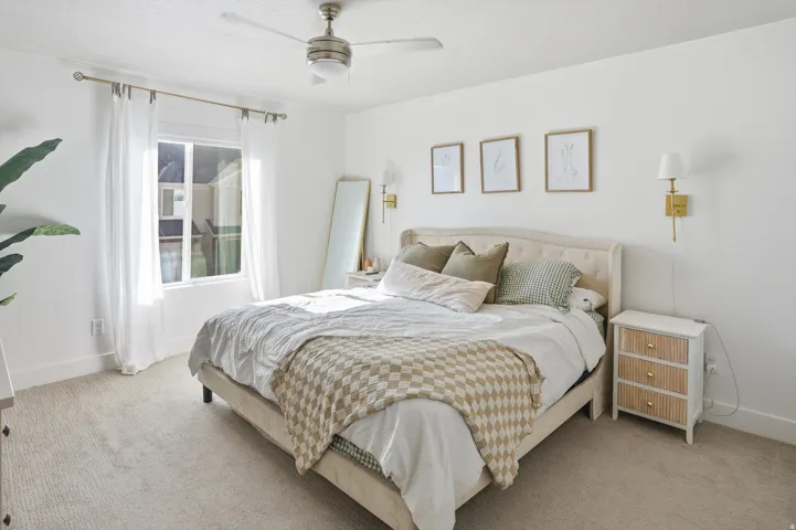 Recessed window with white drapes, ceiling fan with integrated lighting, wall-mounted sconces, and neutral tone carpeting