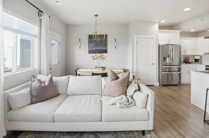 Open-concept living space with wood-finish flooring, white cabinetry, a stainless steel refrigerator, and a gold-tone chandelier