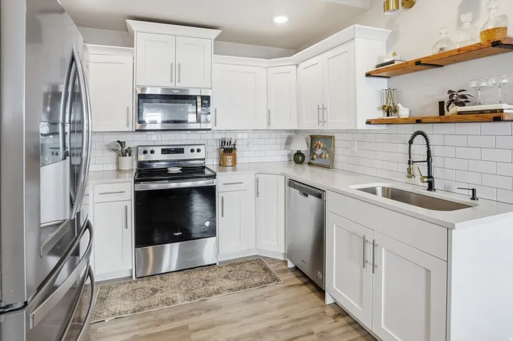 White shaker cabinetry, subway tile backsplash, stainless steel appliances, wood-finish flooring, and open shelving