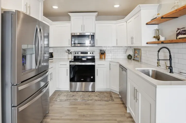 Modern kitchen featuring white cabinetry with stainless steel hardware, stainless steel appliances including French-door refrigerator and built-in microwave, white subway tile backsplash, wood-finish flooring, and a chef's sink with pull-down faucet