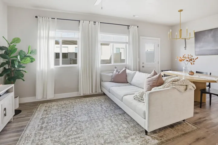 Open-concept living space featuring wood-finish flooring, multiple windows with blinds, a ceiling fan, and a gold-finish chandelier