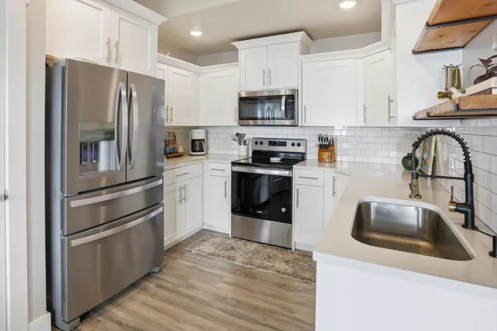 White cabinetry with crown molding, stainless steel appliances, white subway tile backsplash, solid surface countertops, and wood-finish flooring