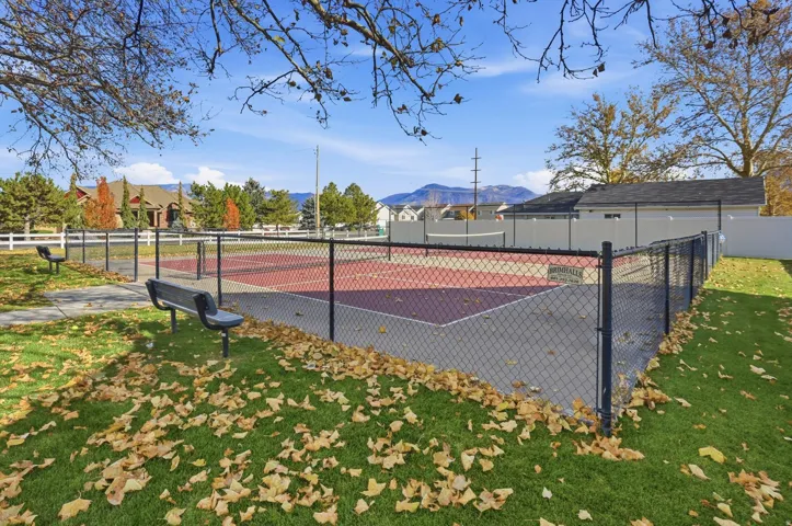 Fenced recreational court with an asphalt surface, surrounded by green lawn and paved walkways