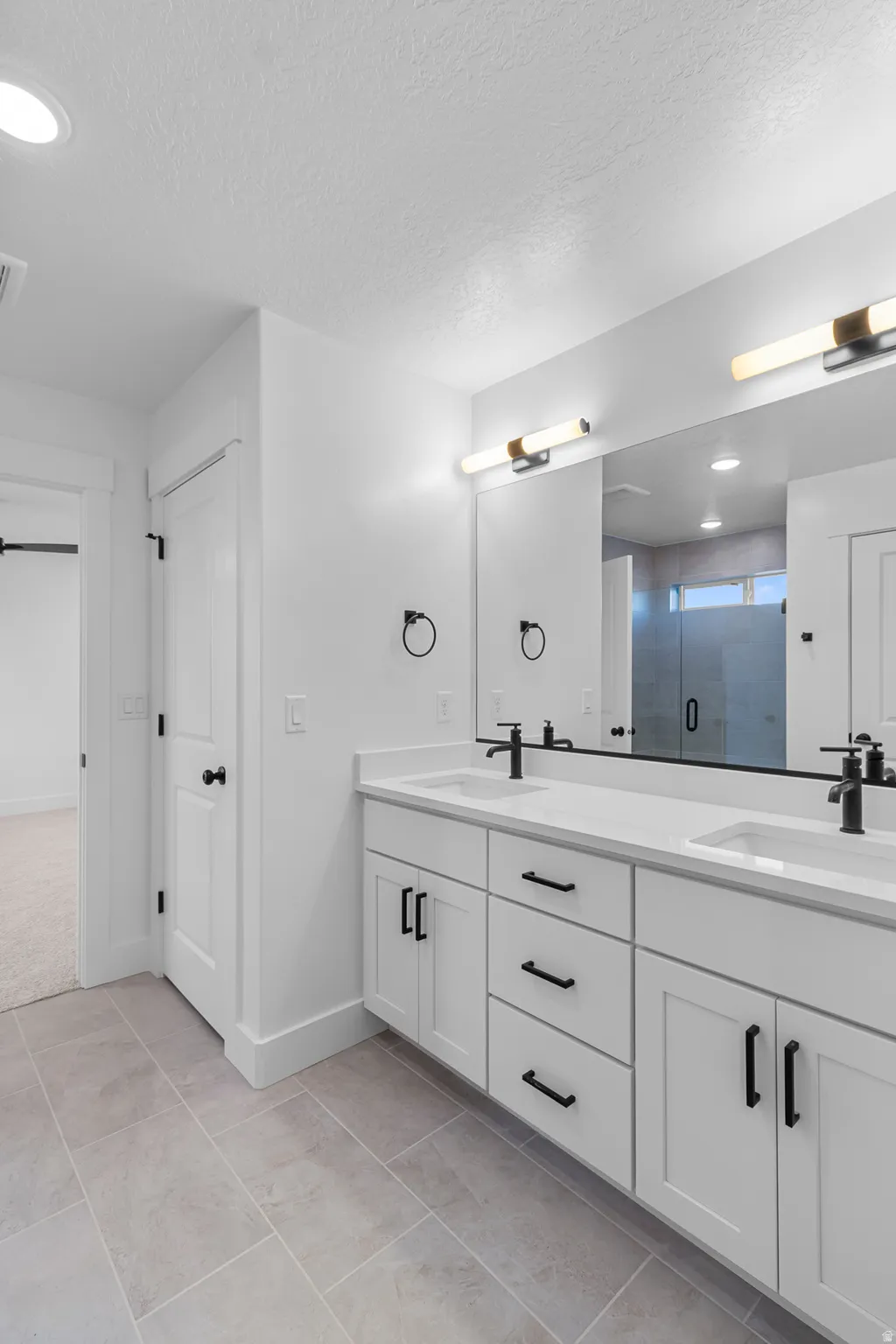 Dual vanity with white shaker-style cabinetry, matte black hardware, and integrated sinks with black faucets