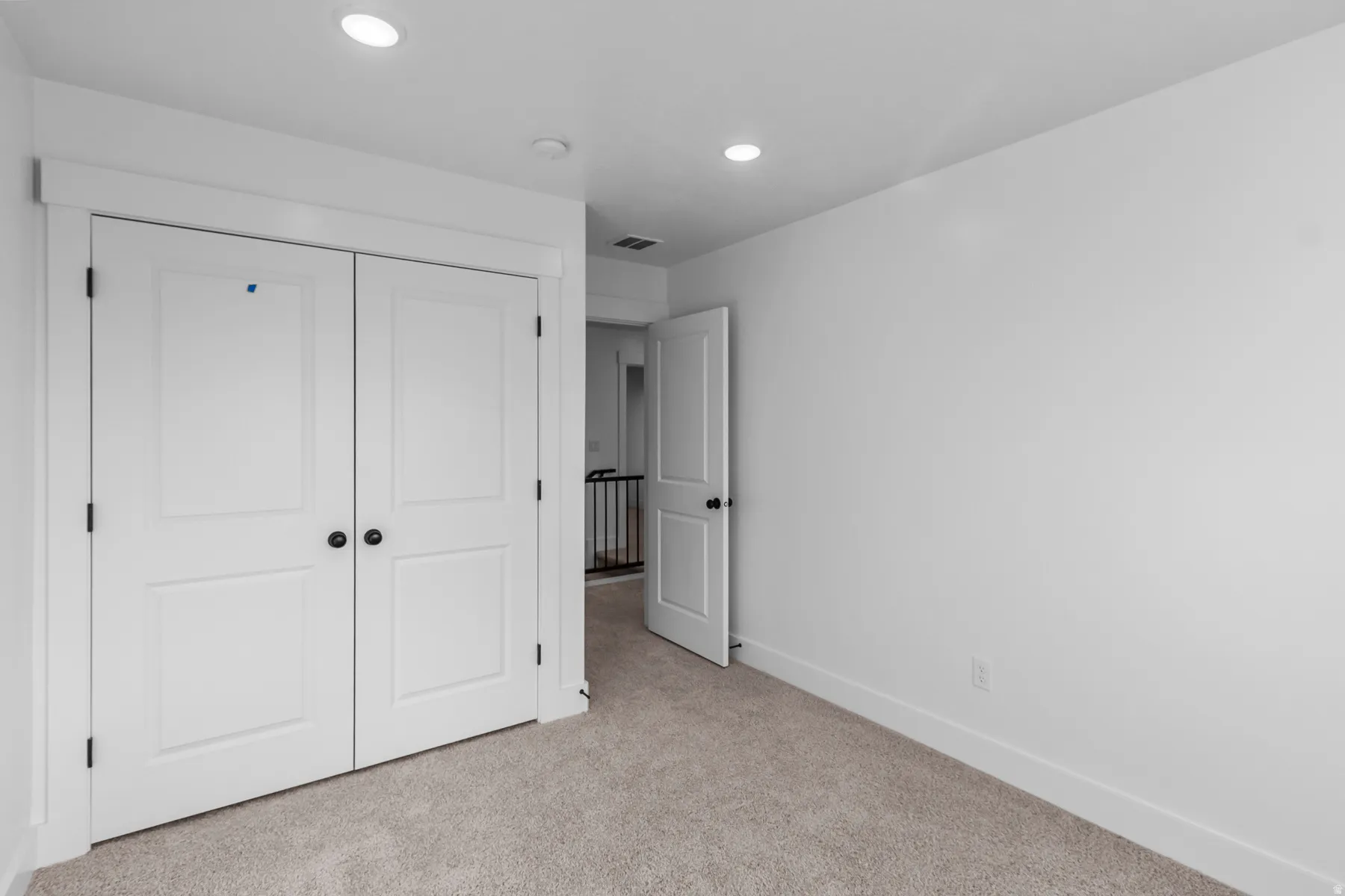 Spacious bedroom with dual white panel closet doors, neutral carpeting, recessed ceiling lighting, and generous wall space ideal for furniture arrangement