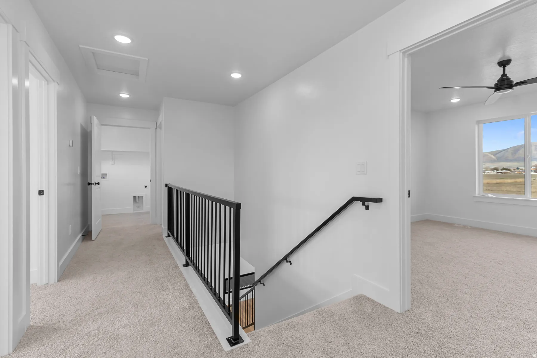 Carpeted hallway with a modern black metal railing, recessed lighting, and a white interior door