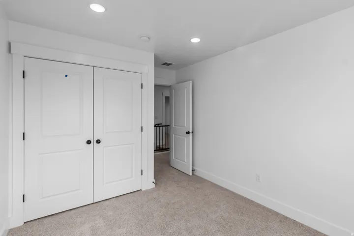 Spacious bedroom with dual white panel closet doors, neutral carpeting, recessed ceiling lighting, and generous wall space ideal for furniture arrangement