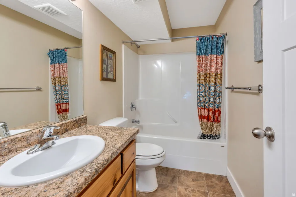 Spacious bathroom featuring a granite-topped vanity with an undermount sink, wood-finish cabinetry, and brushed nickel hardware