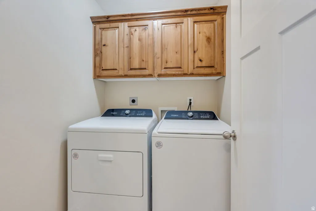 Dedicated laundry room featuring side-by-side washer and dryer with stacked configuration, upper wood-finish cabinetry with recessed panel doors, and neutral wall finishes for convenient in-home garment care