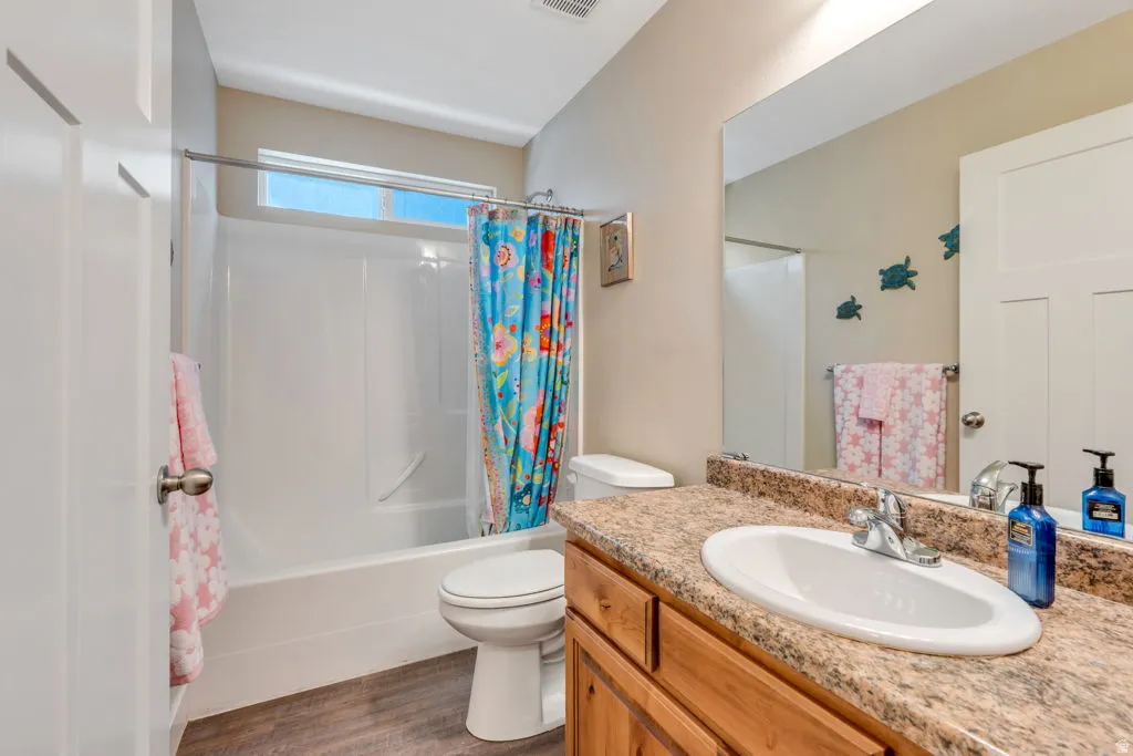 Bathroom featuring a white bathtub and shower combination, wood-finish flooring, a vanity with a surface-mounted sink, and a large mirror