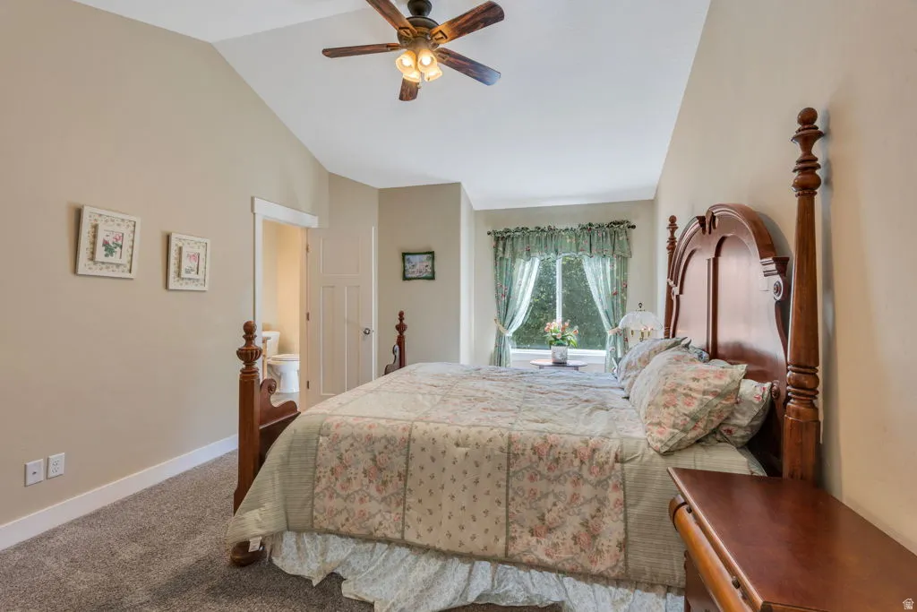 Spacious master bedroom featuring a four-poster wood bed frame, carpet flooring, and vaulted ceiling with ceiling fan