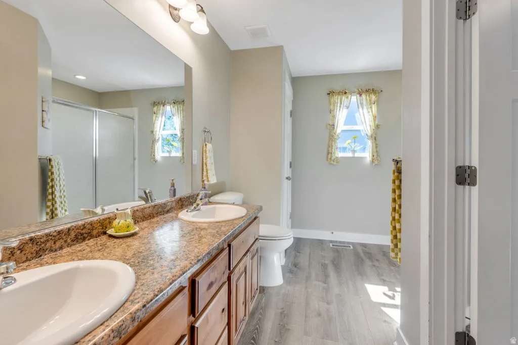 Spa-inspired primary bathroom featuring dual vanities with warm-toned stone countertops, white ceramic vessel sinks, and rich wood cabinetry