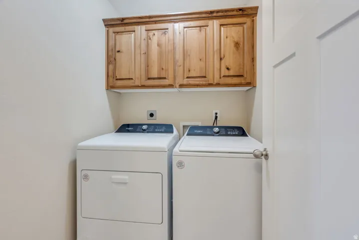 Dedicated laundry room featuring side-by-side washer and dryer with stacked configuration, upper wood-finish cabinetry with recessed panel doors, and neutral wall finishes for convenient in-home garment care
