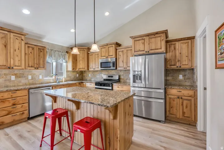 Kitchen featuring wood cabinetry, stainless steel appliances, a center island with a stone countertop, a tile backsplash, and wood-finish flooring