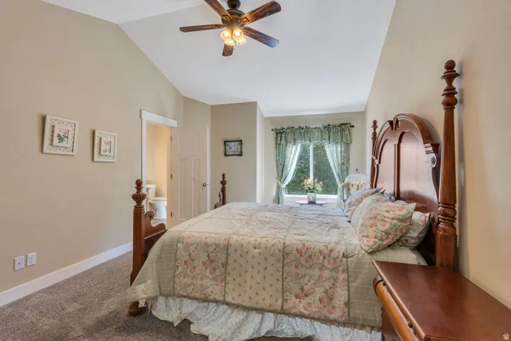 Spacious master bedroom featuring a four-poster wood bed frame, carpet flooring, and vaulted ceiling with ceiling fan