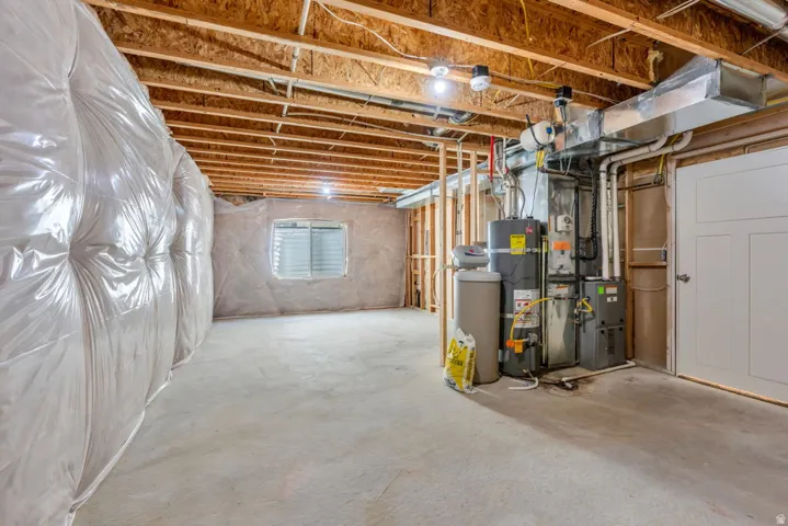 Unfinished basement with exposed wood joists, concrete flooring, and a window with horizontal blinds