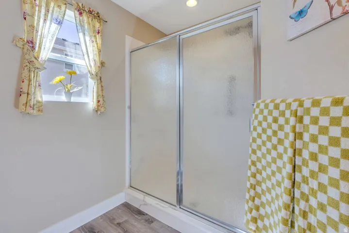Frosted glass shower enclosure with chrome framing, recessed ceiling lighting, and wood-finish flooring