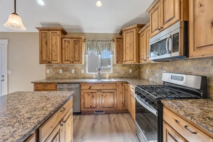 Kitchen featuring wood-finish cabinetry, stone countertops, a tile backsplash, and stainless steel appliances