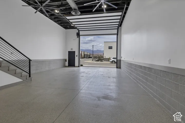 Polished concrete flooring, exposed ceiling structure, industrial-style ceiling fans, roll-up door, and metal staircase railing