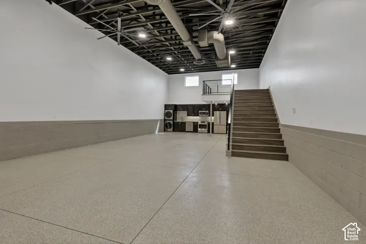 Expansive open space featuring high ceilings with exposed ductwork, large ceiling fans, wood-finish stairs, and a built-in kitchenette with stainless steel appliances