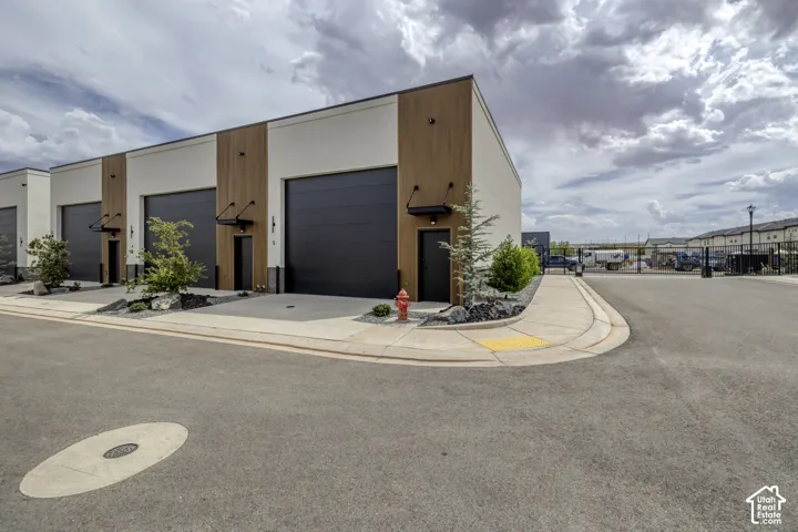 Modern building exterior with wood-finish and neutral-toned siding, large dark roll-up doors, and individual entry doors with awnings
